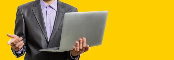 Working with joy. Handsome young man using his laptop and looking at camera with smile while standing against yellow background photo