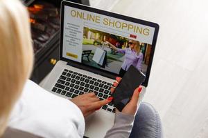 concepto de compras en línea. vista trasera de una chica usando una laptop, mirando el sitio web, sosteniendo una tarjeta de crédito, sentada en casa foto