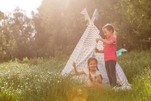Two happy little kids are sitting on the grass and reading fairy tales near a tent in their home yard. Home camping vacation concept photo