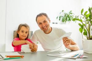 Handsome father and his cute little daughter are playing with paper planes and smiling while spending time together photo