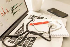 Stethoscope with clipboard and Laptop on desk,Doctor working in hospital writing a prescription. Healthcare and medical concept, test results in background, selective focus photo