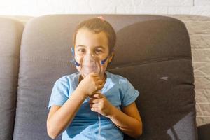 Little caucasian girl is breathing with special mask, which helps to stop asthma attack or relieve symptoms of respiratory disease. photo