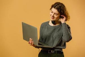 Ecstatic  woman with nude make-up holding headphones and enjoying music during break in office. Indoor portrait of stylish lady resting on the table near computer and waving hands photo