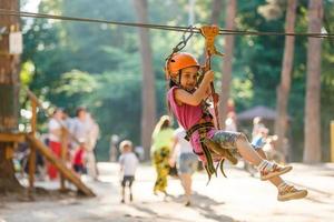 Niña de la escuela feliz disfrutando de la actividad en un parque de aventura de escalada en un día de verano foto