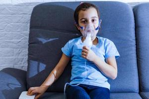 Little caucasian girl is breathing with special mask, which helps to stop asthma attack or relieve symptoms of respiratory disease. photo