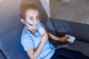 Little caucasian girl is breathing with special mask, which helps to stop asthma attack or relieve symptoms of respiratory disease. photo