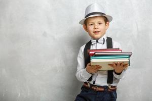 Back to school. Funny little boy in glasses pointing up on blackboard. Child from elementary school with book and bag. Education. Kid with a book photo