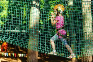 Adorable little girl enjoying her time in climbing adventure park on warm and sunny summer day photo