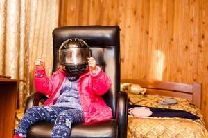 little girl in a motorcycle helmet in a chair at home photo