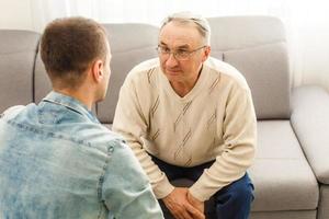 Young man sitting on a sofa smiling and talking with his grandfather photo