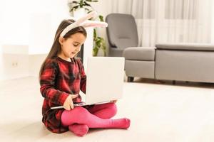 niña pequeña con su conejito usando la computadora juntos preparándose para la profundidad de campo poco profunda de pascua foto