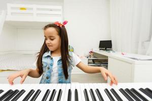 Cute little girl plays on piano, synthesizer. Training. Education. School. Aesthetic training. Elementary classroom. photo