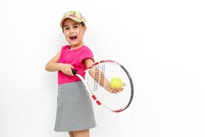 Full length studio photo of seven year old girl holding tennis racket and tennis ball isolated on white