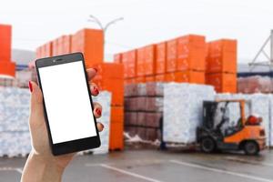 Hand holding smartphone against warehouse worker loading up pallet photo