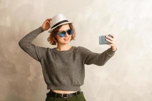 Portrait of cool cheerful girl having video-call with lover holding smart phone in hand shooting selfie on front camera isolated on background enjoying weekend vacation photo