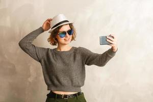 retrato de una chica alegre y fresca que tiene una videollamada con un amante que sostiene un teléfono inteligente en la mano disparando selfie en la cámara frontal aislada en el fondo disfrutando de las vacaciones de fin de semana foto