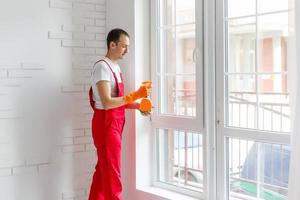 Male janitor cleaning a window in an office wearing an apron and gloves as he works photo