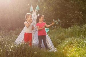 Two happy laughing little girls in camping tent in dandelion field photo