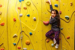 Bouldering, little girl climbing up the wall photo