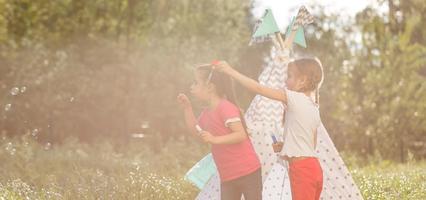 Two happy laughing little girls in camping tent in dandelion field photo