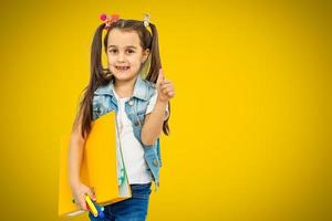Portrait of stylish little girl with finger pointed up. Little child in striped shirt has idea. Kid isolated on yellow blackboard. Success, bright idea, creative ideas and innovation technology concep photo