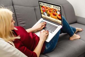 Woman lying on sofa and holding phone with app delivery food screen photo