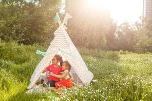 Two happy laughing little girls in camping tent in dandelion field photo