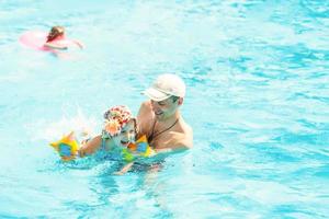 Little girl learning how to swim with swimming instructor. Happy smiling father and daughter relaxing in a swimming pool in a resort. Relaxed child floating in swimming pool with her dad photo