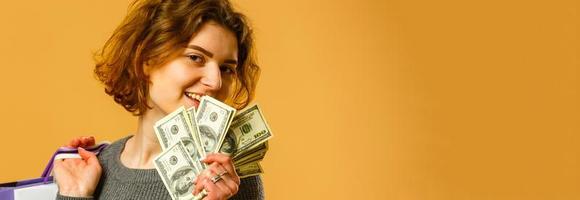 Photo of cheerful pretty young woman standing isolated over yellow wall background. Looking aside holding shopping bags.