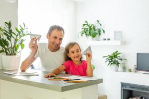 Handsome father and his cute little daughter are playing with paper planes and smiling while spending time together photo
