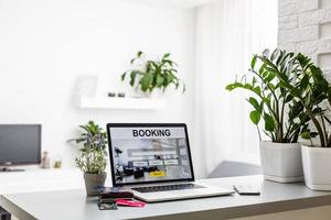 laptop with hotel booking screen on table near phone and flower photo