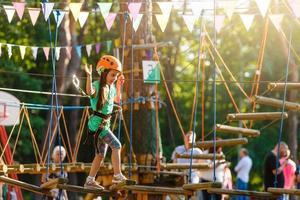 adorable niña disfrutando de su tiempo en el parque de aventuras de escalada en un cálido y soleado día de verano. actividades de verano para niños pequeños. niño divirtiéndose en vacaciones escolares. foto