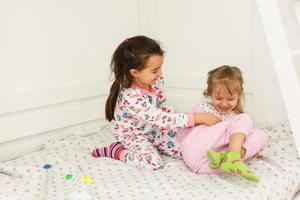 Two sisters, wearing white pajamas, on the bed and have fun. Concept of youth, wellness and health, happiness and freedom. photo