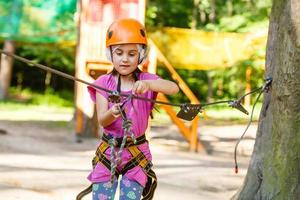 Adorable little girl enjoying her time in climbing adventure park on warm and sunny summer day. Summer activities for young kids. Child having fun on school vacations. photo