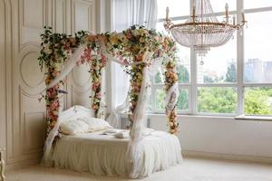 white bed. white bed in a classic style with a garland of leaves and flowers. the spring location. decorated in a spring decor. the white four-poster bed is decorated with flowers photo