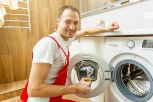Young attractive smiling worker in uniform fixing washing machine, background photo