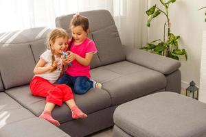 gente, niños, tecnología, amigos y concepto de amistad - niñas felices sentadas en el sofá y tomándose selfie con un smartphone en casa. foto