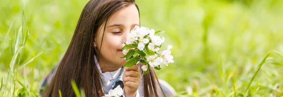 Beautiful little girl lying on the field in green grass and blowing dandelion. Outdoors. Enjoy Nature. Healthy Smiling Girl on spring lawn. Allergy free concept. Freedom photo