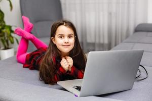 Happy little girl at home working with a laptop photo