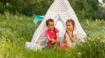 childhood and hygge concept - happy little girls playing in kids tent photo