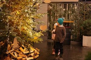 hermano con hermana divirtiéndose cerca del árbol de navidad iluminado al aire libre por la noche. foto