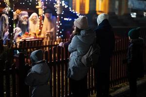 Family against scene where the Virgin Mary gave birth to Jesus and he lies in the cradle surrounded by people who have come to celebrate the Nativity of Christ. photo