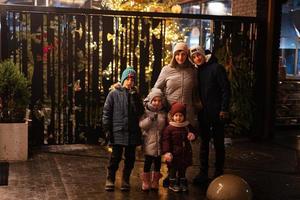 Mother with four kids stand against illuminated Christmas tree outdoor in evening. photo