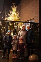 madre con cuatro hijos se opone al árbol de navidad iluminado al aire libre por la noche. foto