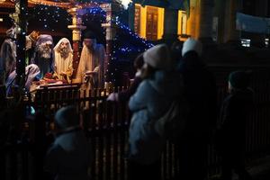 Family against scene where the Virgin Mary gave birth to Jesus and he lies in the cradle surrounded by people who have come to celebrate the Nativity of Christ. photo