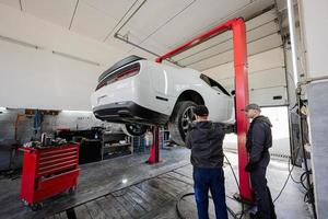 Two mechanic in service repair station working with muscle car in lift. photo