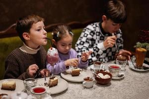 Kids eating desserts together at cozy cafe and having fun.  Boy drink milkshake. photo