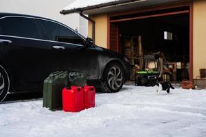 Four canisters with gasoline stand in snow against car. photo