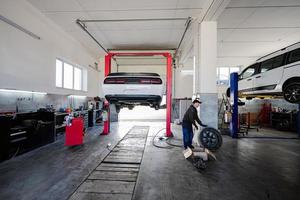 Mechanic in service repair station working with muscle car, dismantles a wheel on lift. photo