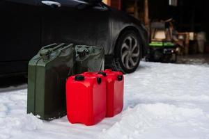 Four canisters with gasoline stand in snow against car. photo